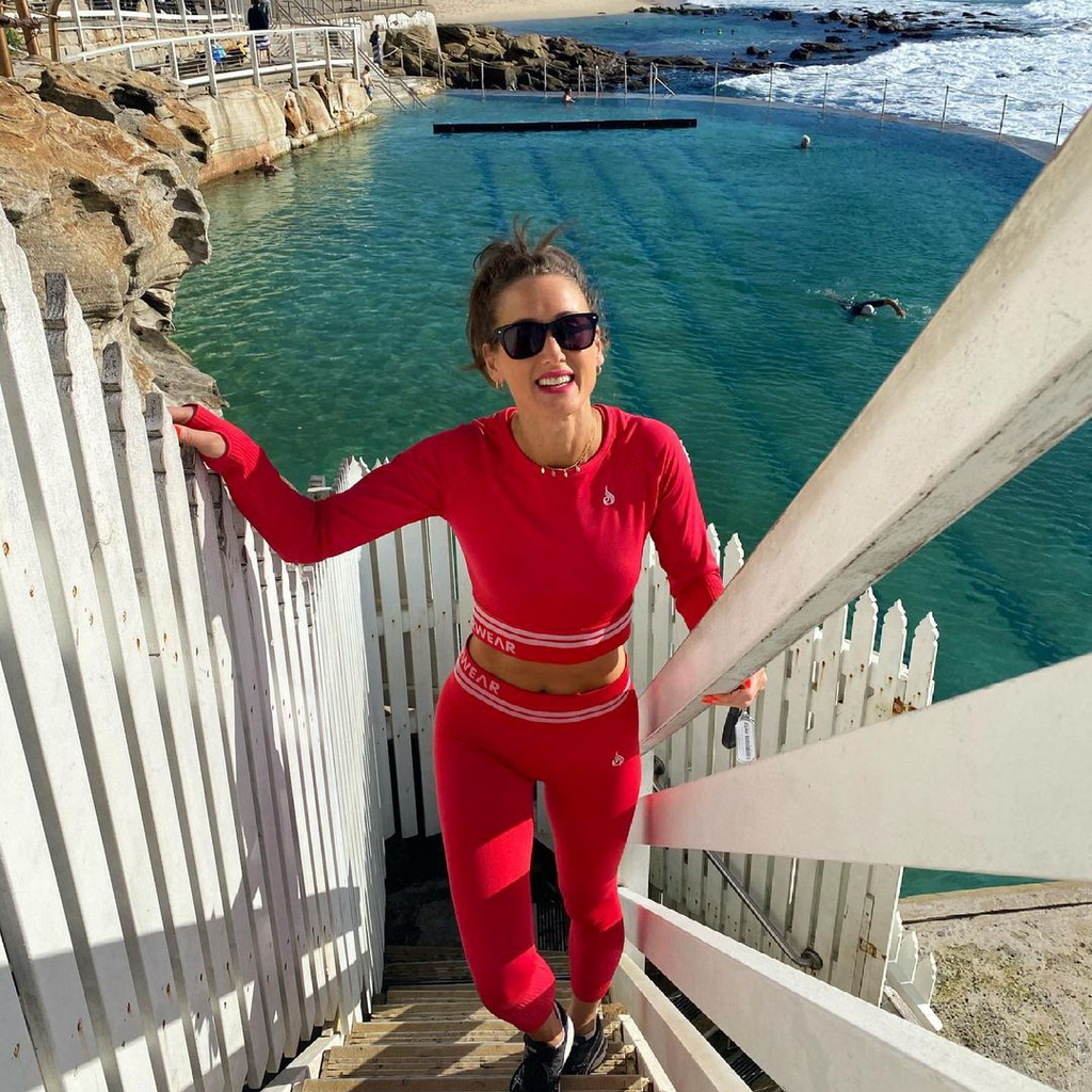 A photo of Jomeis Fine Foods' founder, Vicki Nguyen, climbing a beach staircase. She is wearing red activewear and black sunglasses. Behind her you can see the coastline and a lapping wave. 