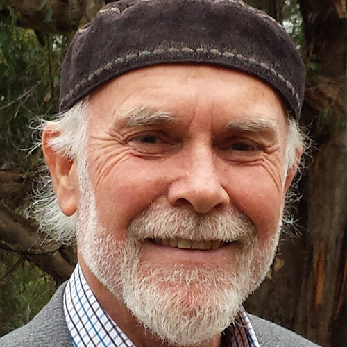 An image of Dr Isaac Golden. He is smiling into the camera. He is wearing a traditional hat and a suit. The image is closeup so only the tops of his shoulders can be seen. Behind him, in the background is a strong tree trunk and some greenery. 