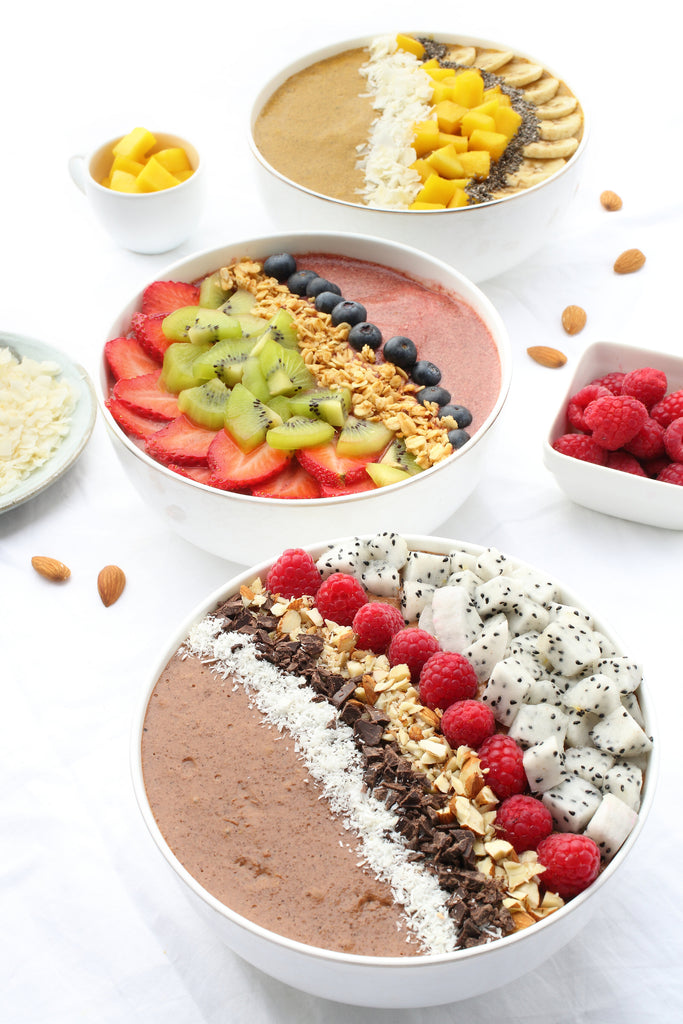 3 Superfood breakfast bowls, one in each flavour. At the front in cacao + coconut, the next is beetroot + cacao and at the back is turmeric + ginger. They are all topped with fruit and nuts 