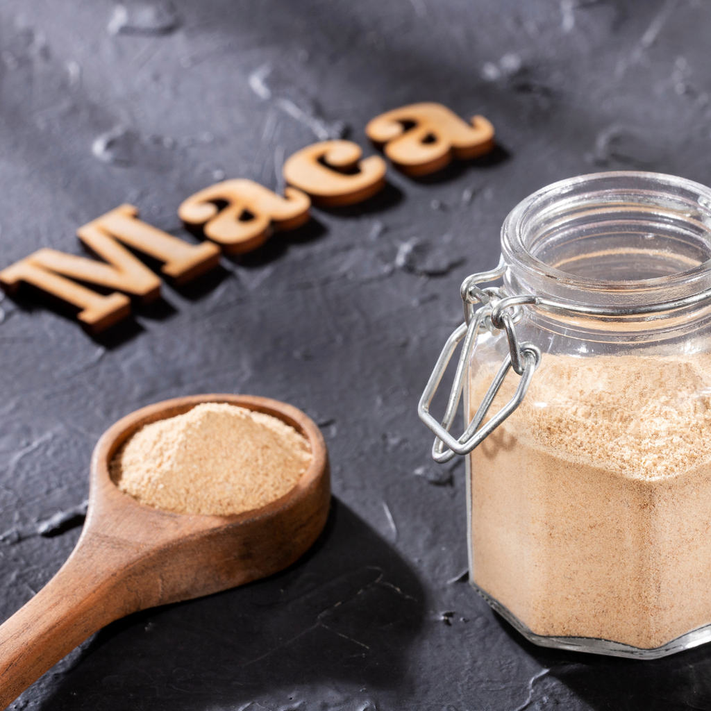 A jar or maca powder. A wooden spoon next to it is also filled with Maca powder.