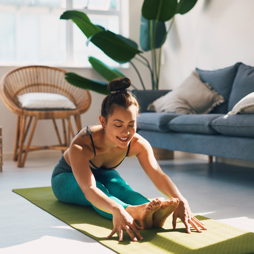 A lady doing yoga at home. She has her legs stretched forward and is bending toward them to reach her toes 