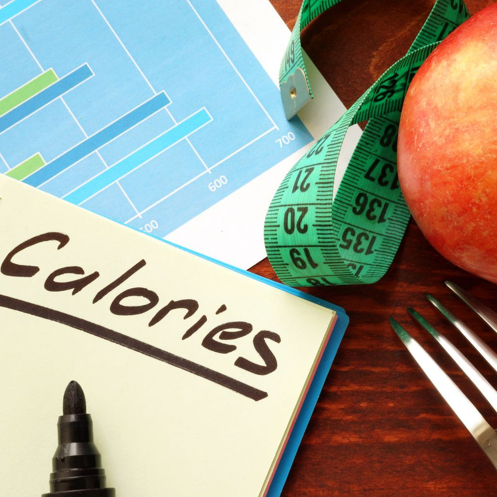 The word calories written on a white board. Next to it is a measuring tape, and apple and a fork.