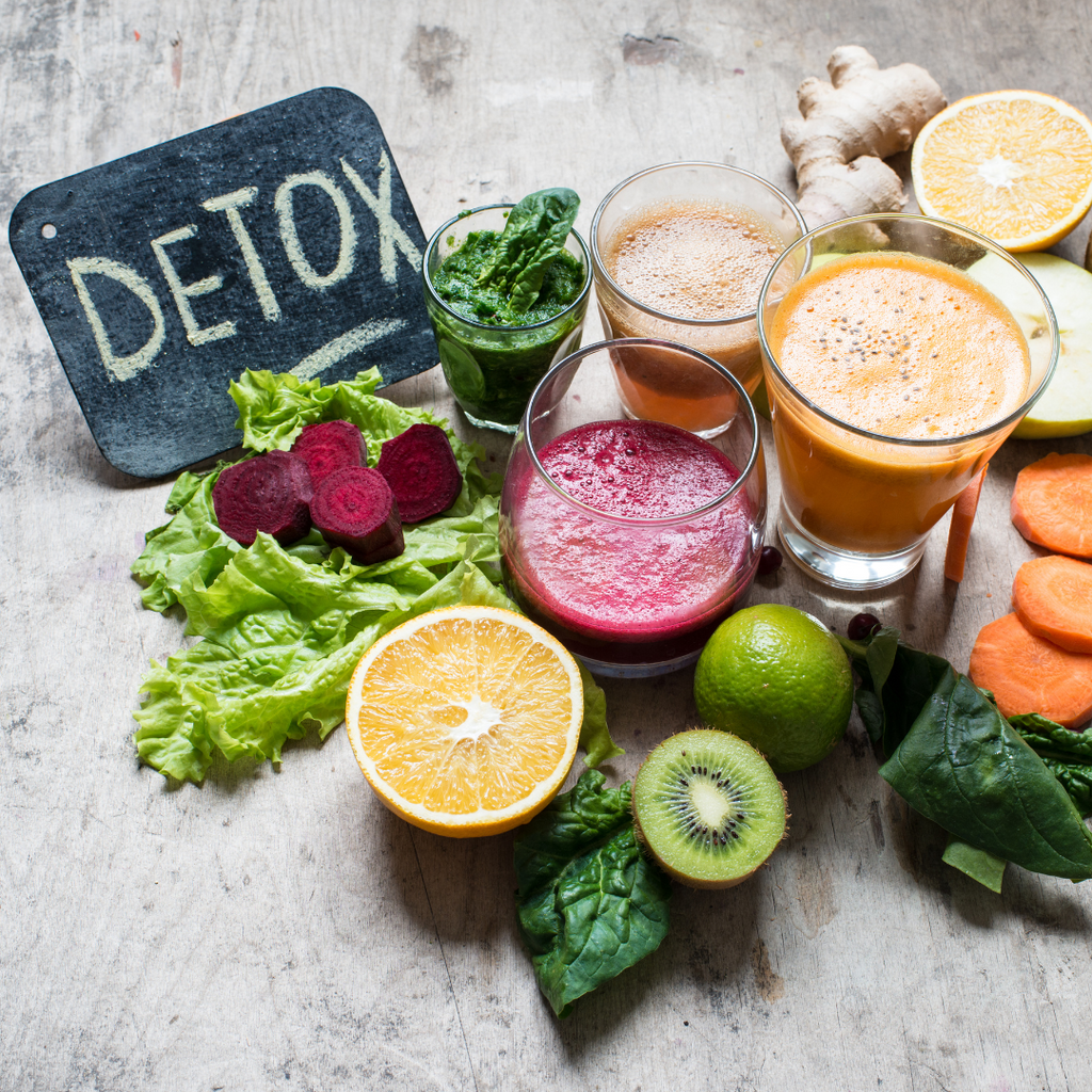 The word detox on a blackboard. Fruits, vegetables and drinks to help detoxing becoming a reality next to it.