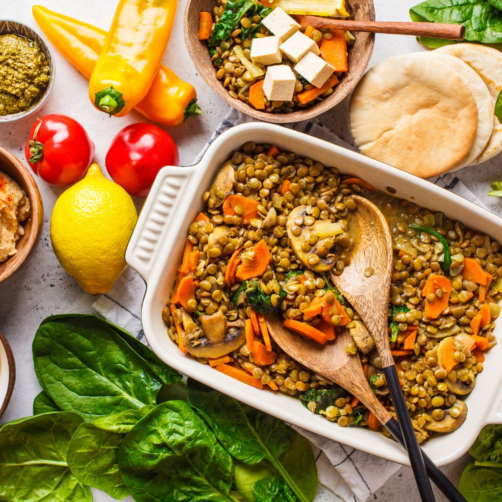 A plant-based dinner in a casserole dish. It is surrounded by lemon, capsicum, carrot, spinach and more. Healthy Eating