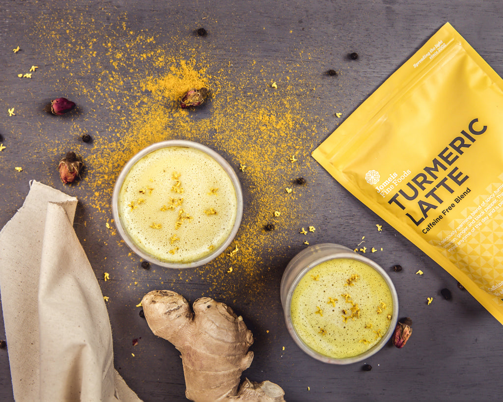 an image of a turmeric latte packet and some turmeric and ginger puddings. The turmeric latte packet is yellow and on the right of the screen . There are two puddings to the left of it. One of the puddings is surrounded by turmeric latte powder. 