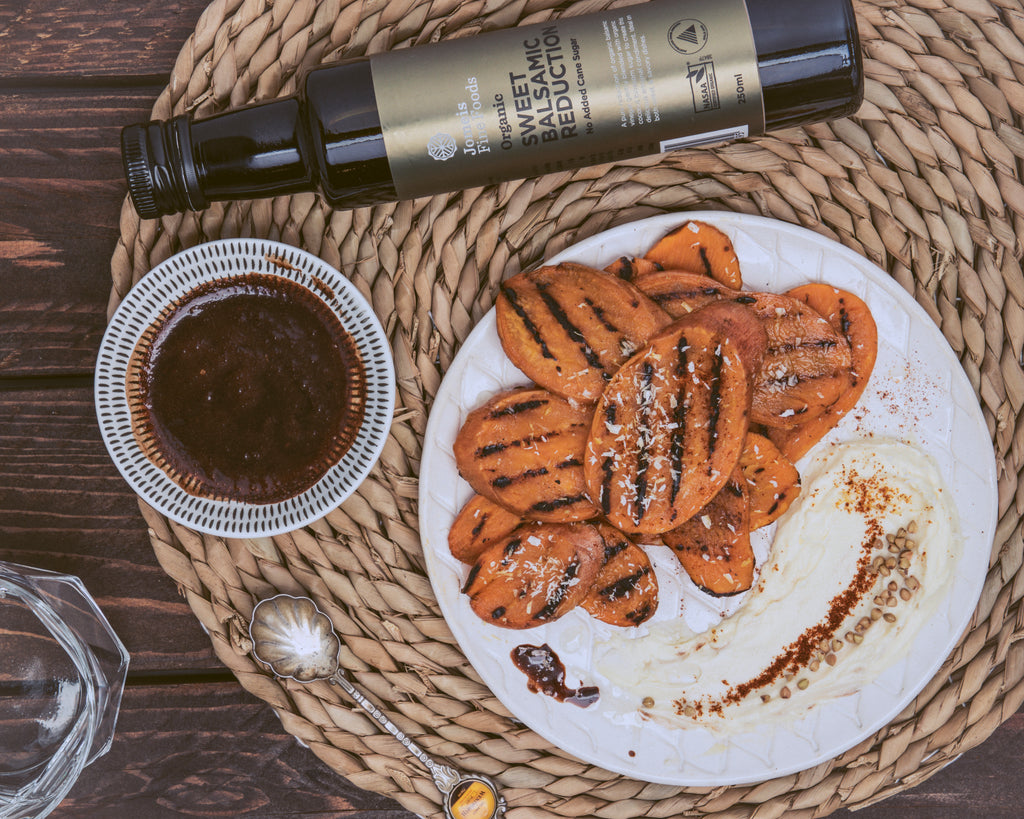 An organic sweet balsamic reduction on a rope placemat. The sweet balsamic reduction is laying across the top of the mat, there are roasted sweet potatoes below it and a dipping cup filled with the balsamic reduction blend beside it. 