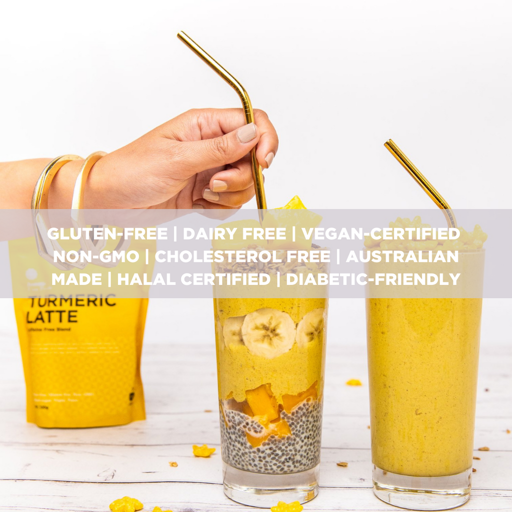 Two cups of turmeric chia pudding with golden reusable straws in them. On the left of the glasses is a woman hand holding one of the straws as though she is inserting it. Behind her arm is a yellow turmeric latte packet. There is some spills on the table