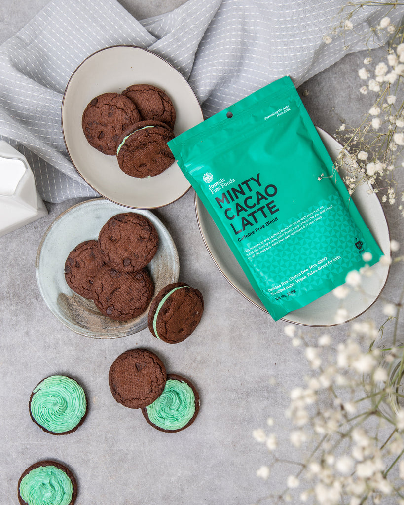 A minty cacao latte packet in the middle of the screen. It is resting on a white plate. it is surrounded by chocolate cookies which are stuck together with aa minty cacao paste. 