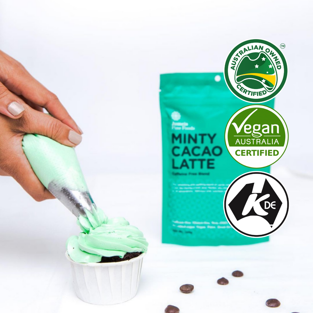 A minty cacao latte packet sits off to the right side of the screen. In front of it are some chocolate chips and to the left are a woman's hands piping mint icing onto a cupcake. 